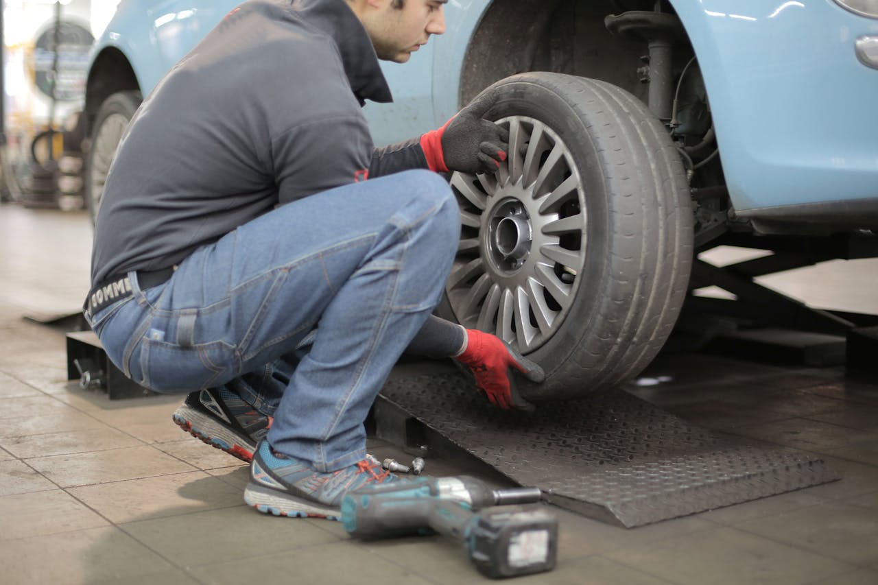 Services-02 Mechanic changing a car tire indoors, using tools for vehicle maintenance.
