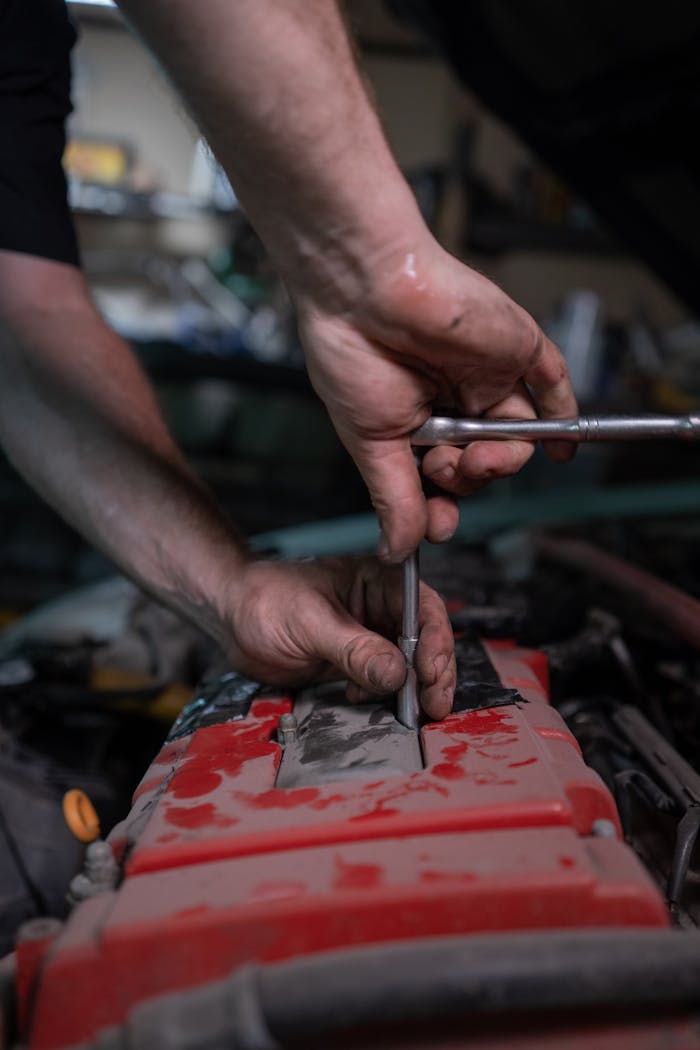 Services-03 A mechanic uses a socket wrench to repair a car engine in a garage setting.